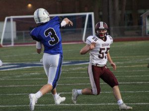 With a Dedham defender in his grill, senior quarterback Holden Ferrari (3) airs a ball out down the sideline to Drew Dummer for a long completion late in the first quarter.