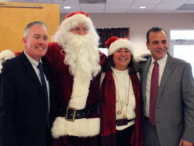 COA director Lina Arena-DeRosa joins Senator Mike Rush and Representative Paul McMurtry for a photo with Santa at the annual COA holiday luncheon.