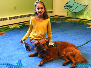 A young Medfielder reads a story to her non-judgmental audience: Toby, a three-year-old mini goldendoodle.