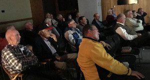 The audience watches a documentary on ‘The Game’ between Harvard and Yale during a lecture at the Needham Library.