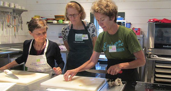 Karen and Maria watch as chef Didi Emmons shows the class a special way to cut garlic.