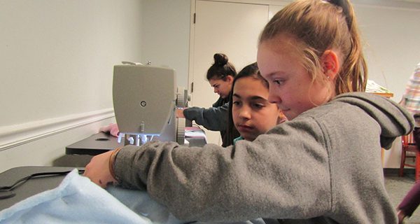 Avery and Eliza, 10, use a sewing machine to stitch together a crate pad.