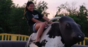 Woman riding a mechanical bull outdoors.